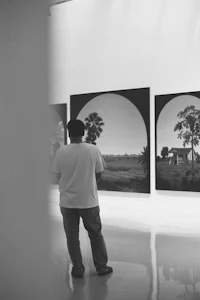 black and white photo of a man looking at paintings in an art gallery