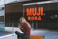 a woman sitting on a bench in front of a muji store