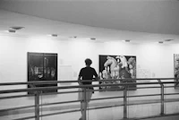 a black and white photo of a woman looking at paintings in a museum