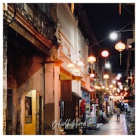 a narrow street with lanterns and people walking down it at night