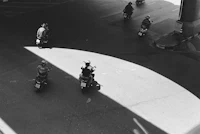 a black and white photo of people riding scooters on a street