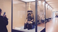 a woman takes a picture of a samurai in a museum