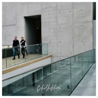two people walking down a walkway in front of a building