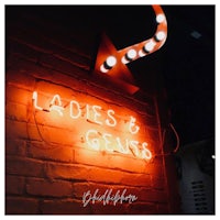 a neon sign that says ladies and gents on a brick wall